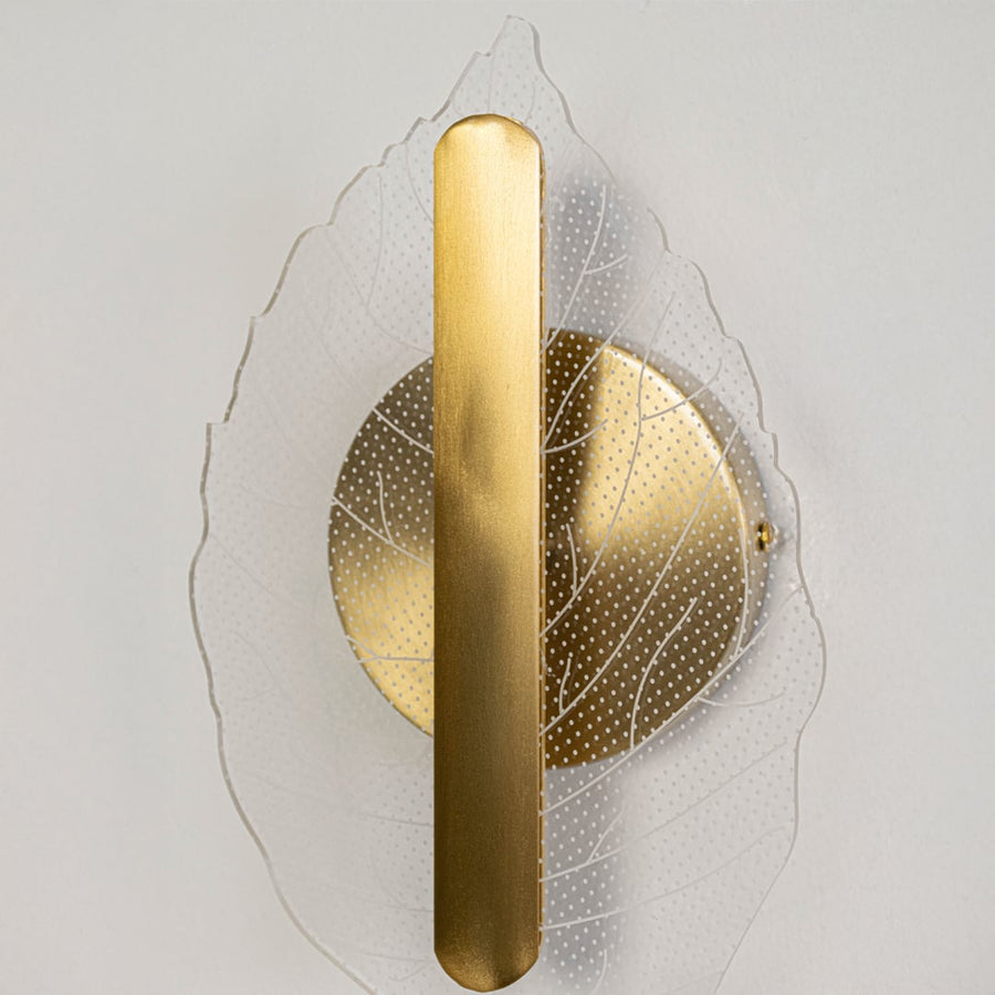 Closeup of gold metal and clear textured glass leaf wall light showing fine detailing for modern decorative home lighting.
