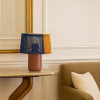 Decorative table lamp with blue and mustard woven shade placed near an armchair adding warm accent lighting to an elegant living space