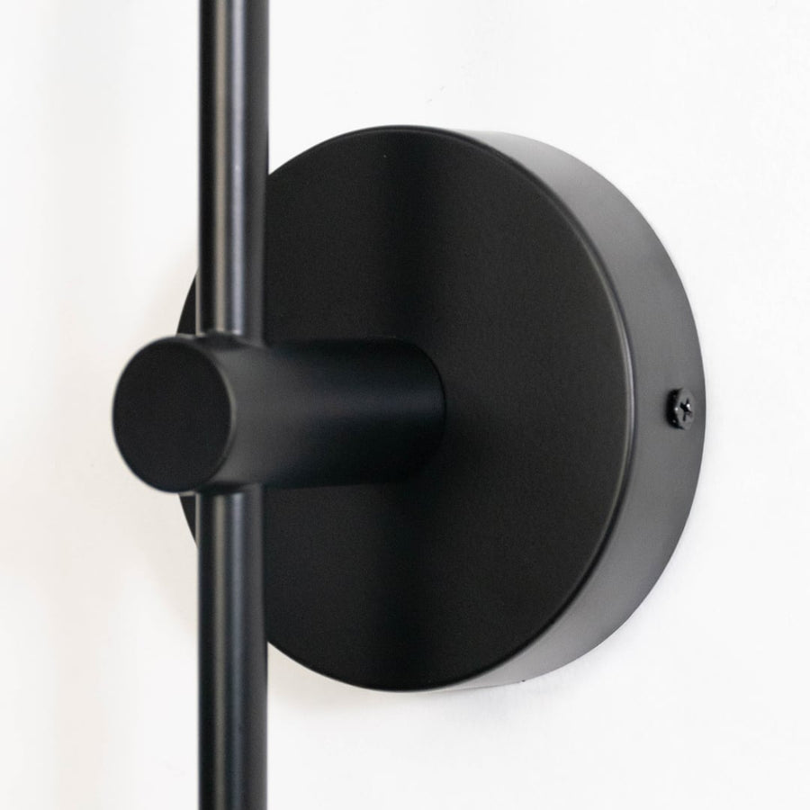 Closeup of modern black wall sconce with cylindrical glass shade sleek metal finish perfect for bedroom living room and hallway.