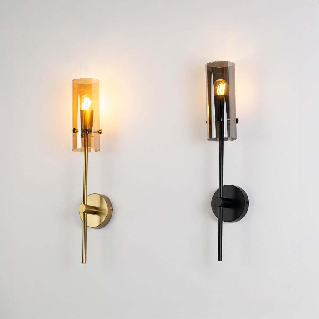 Contemporary wall lights in black and gold finish glowing with cylindrical glass shades for stylish modern home interior décor.