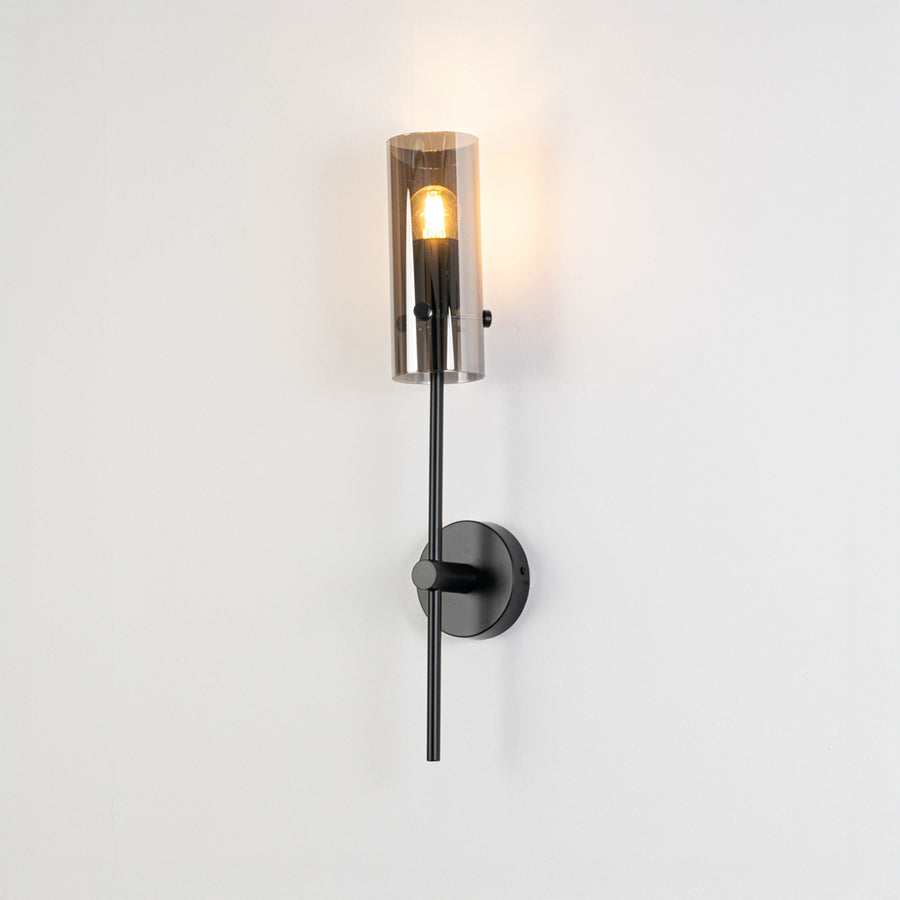 Modern wall light with black metal finish and warm glass shade on neutral wall background sleek vertical design ideal for bedroom living room decor.