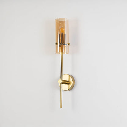 Minimalist gold wall sconce with cylindrical glass shade switched off displayed against plain white background for product view.