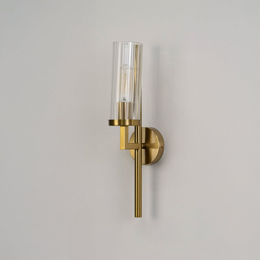 Minimalist gold wall sconce with ribbed cylindrical glass shade switched off against plain white background for product display.
