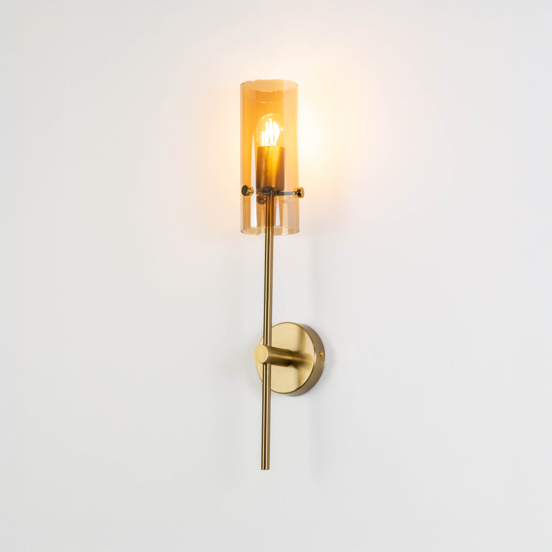 Minimal wall light in gold metal finish with cylindrical glass shade for bedroom or living room decor lighting white background.