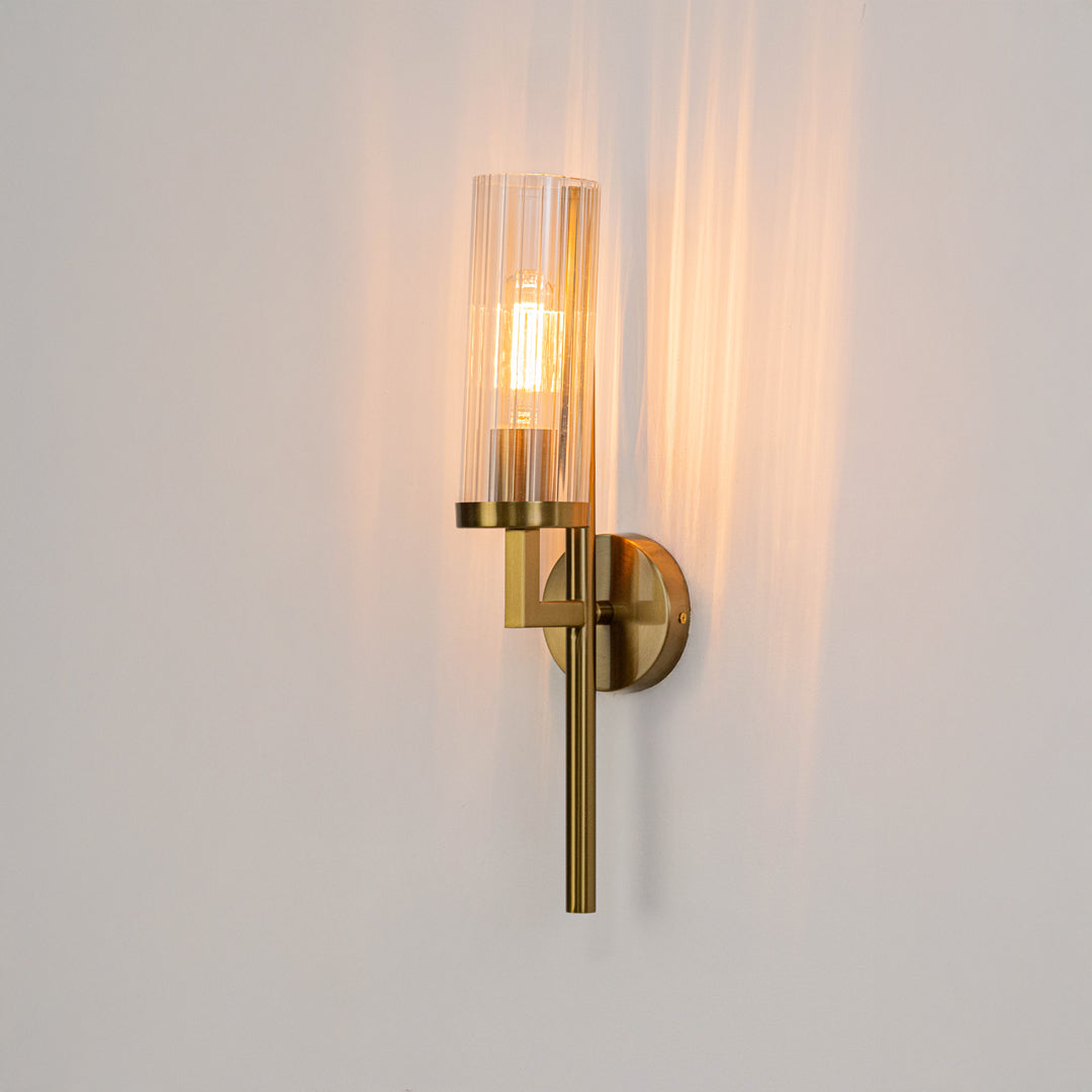 Wall light with gold metal finish and warm glowing glass tube on neutral wall background modern luxury lighting for bedroom living room decor.