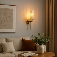 Elegant gold wall sconce with ribbed glass shade glowing warmly in modern living room beside sofa wall art and indoor plant.