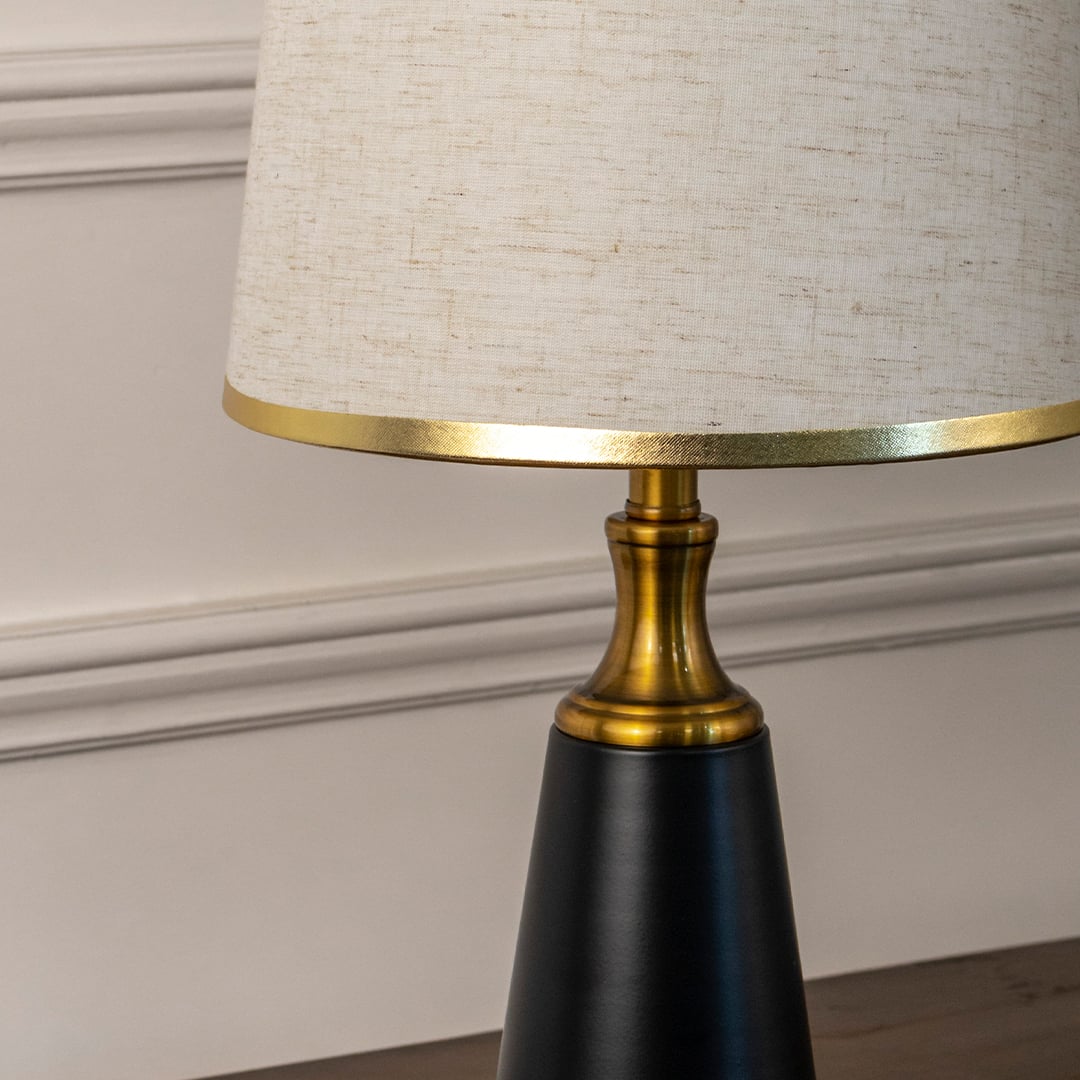 Closeup of designer table lamp featuring matte black base with gold accents and linen shade showcasing its premium detailing.