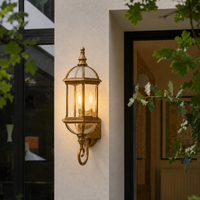 Vintage brass metal arched cage glass column wall sconce on beige stucco exterior entryway facade for home porch lighting.