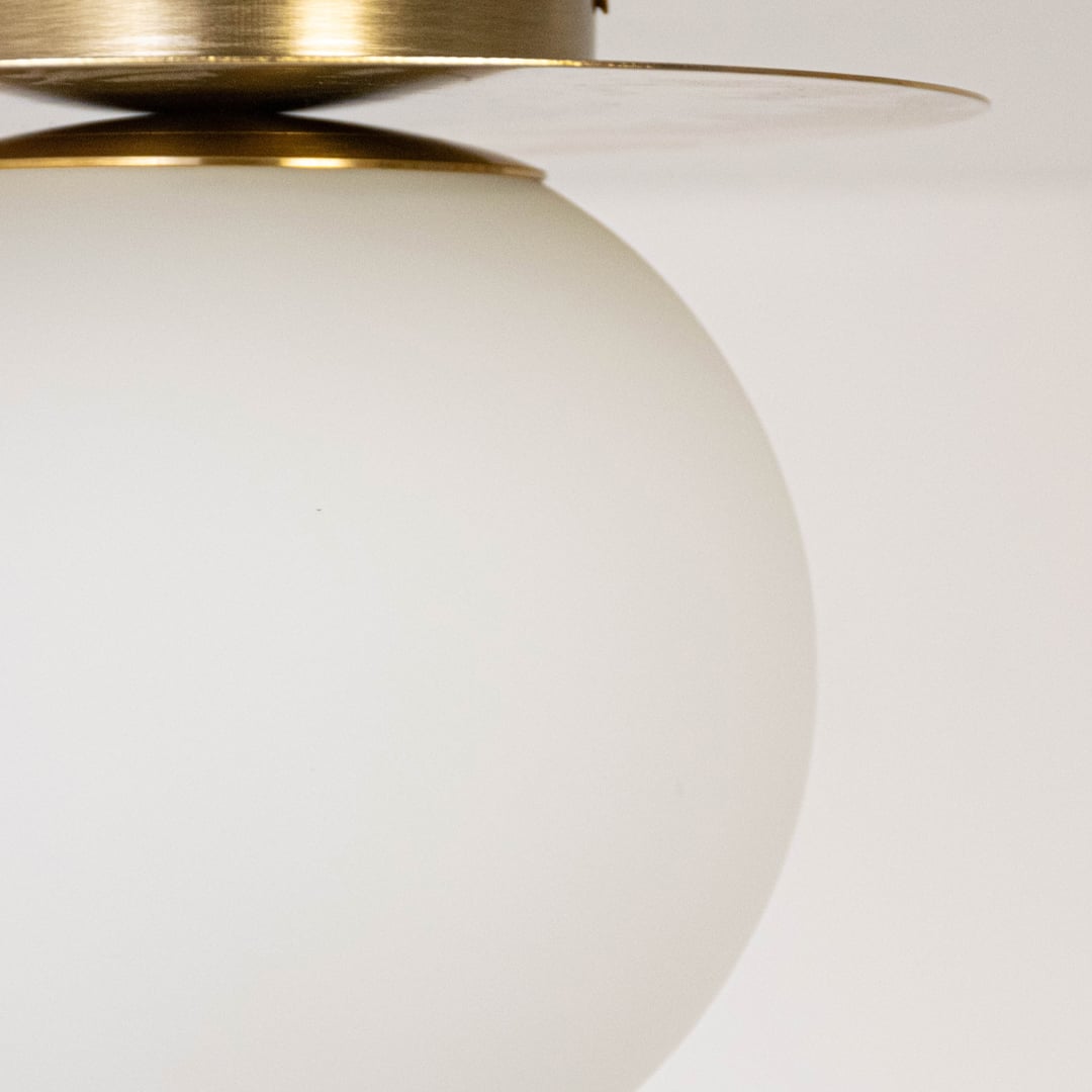 Closeup of ceiling light with brushed gold base and frosted glass globe shade for modern home lighting decor.