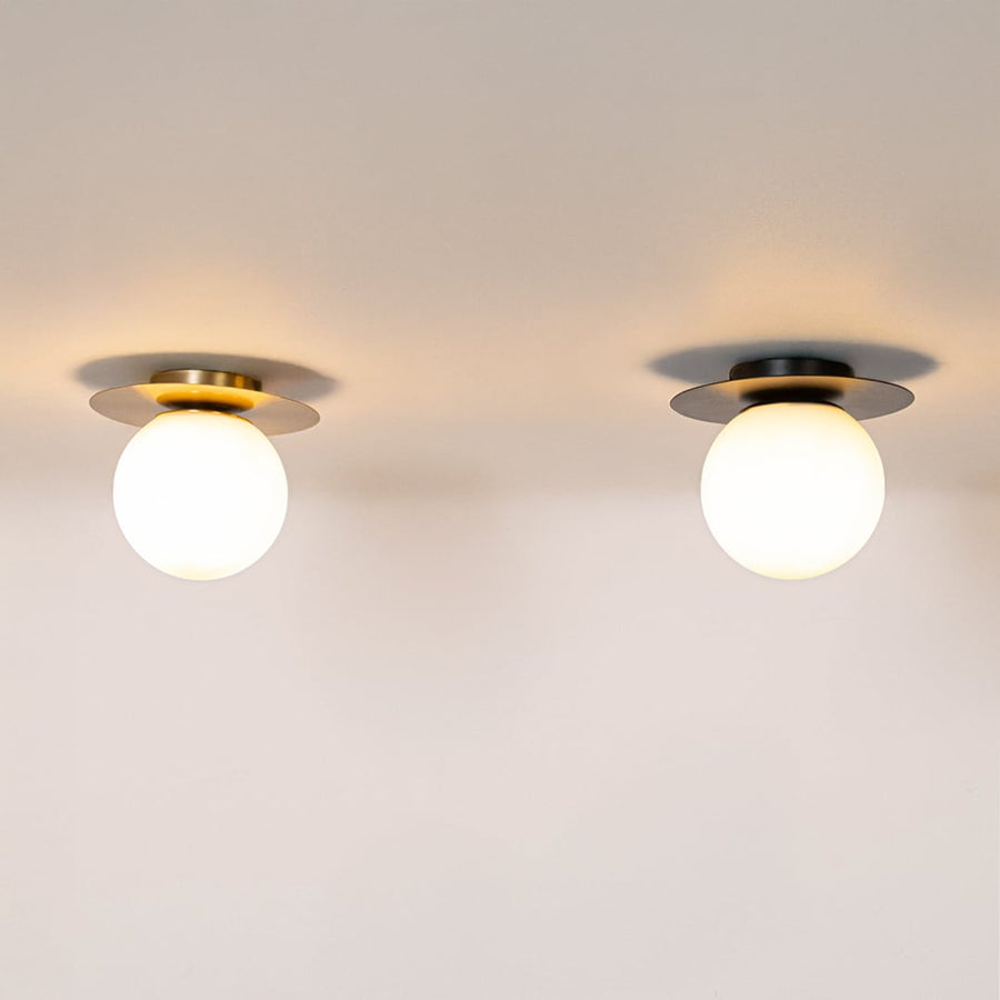 Set of ceiling lights in brushed gold and black finish with frosted glass globe shades glowing on white background.