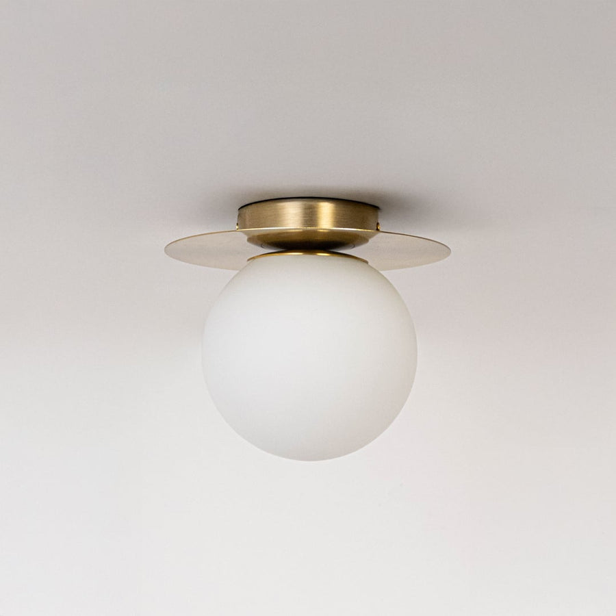 Ceiling light with brushed gold finish base and frosted glass globe shade shown off on plain white background.