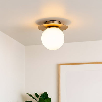 Modern ceiling light with brushed gold base and frosted glass globe styled in room interior for warm home lighting.