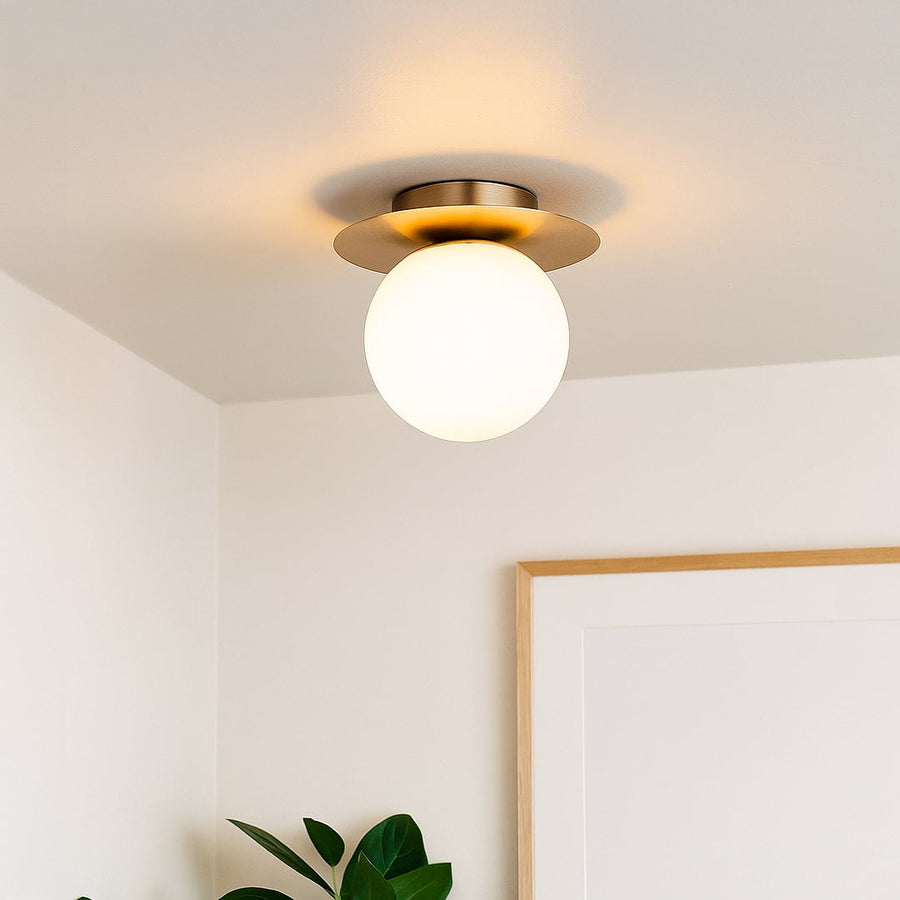 Modern ceiling light with brushed gold base and frosted glass globe styled in room interior for warm home lighting.