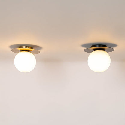 Set of ceiling lights in black and gold finish with frosted glass globe shades glowing on plain white background.