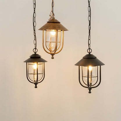 Three outdoor pendant lanterns with lights on displayed together in various metal finishes creating a warm illuminated arrangement on a plain background.