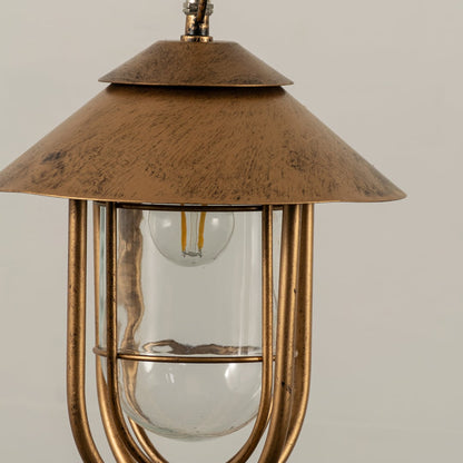 A focused closeup of the lantern showing its textured metal top and inner glass cylinder with detailed craftsmanship visible in the curved supporting frame.