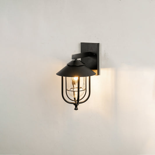 Industrial black metal cage outdoor wall sconce on white background with clear glass shade casting a warm porch glow.
