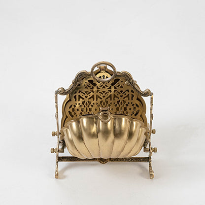 Angled view of the gold brass shell biscuit warmer showing the folding mechanism and decorative stand on a plain white studio background setting.
