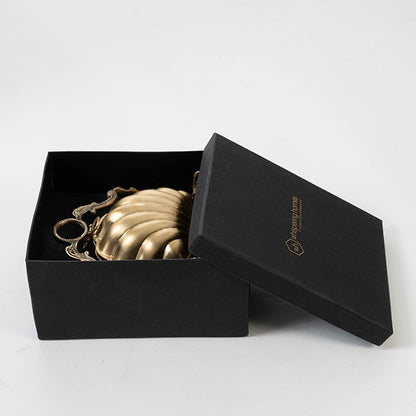 Gold brass shell biscuit warmer in a black box showing decorative stand on a plain white studio background setting.