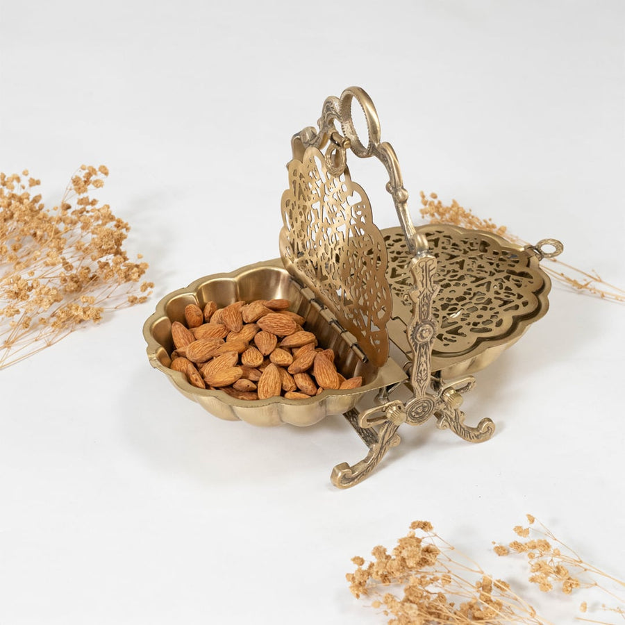Elegant gold metal shell shaped holder placed on a placemat next to a brass goblet and fruit bowl in a dining room for a luxurious interior look.