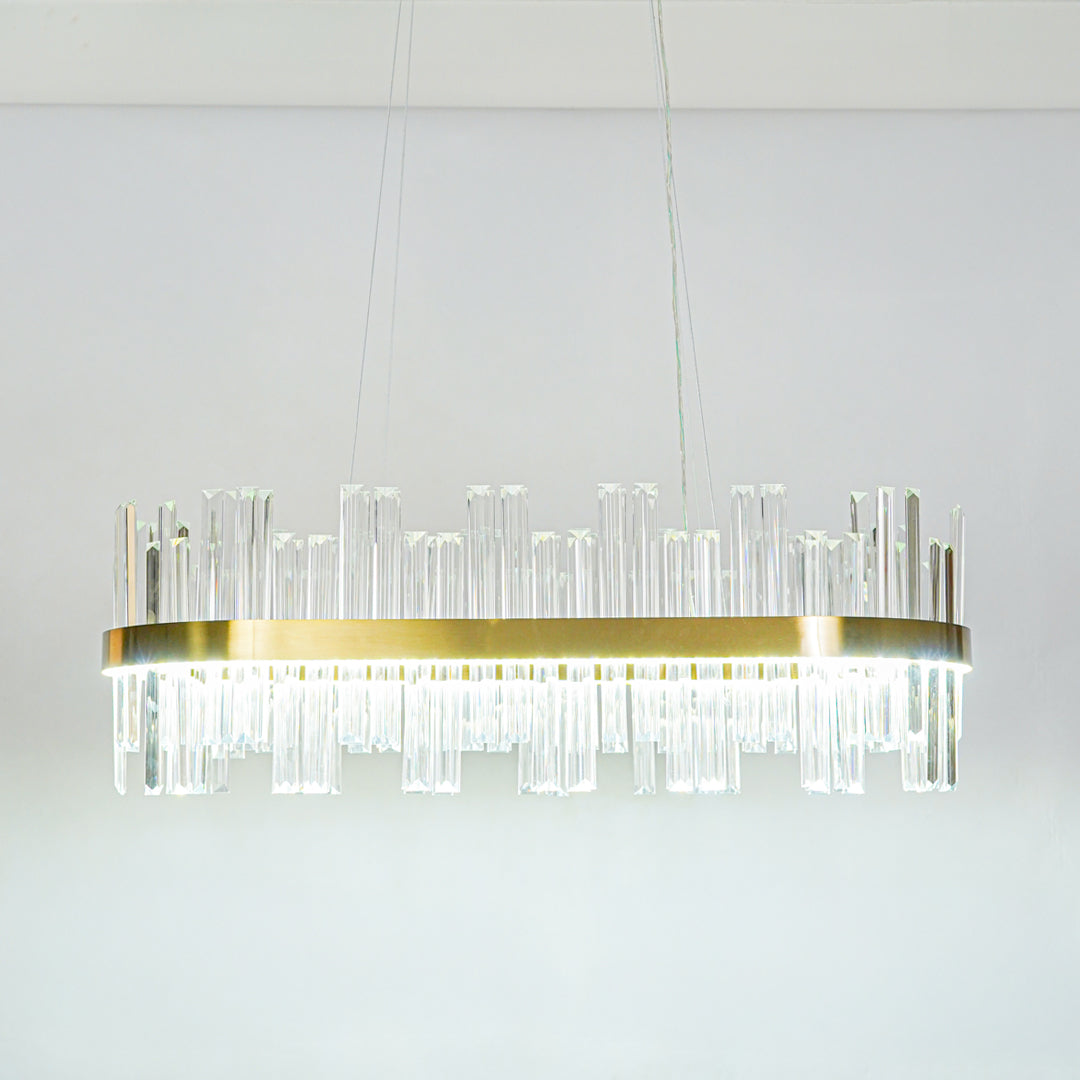 Minimal long crystal bar chandelier with transparent glass elements and gold finish suspended against clean ceiling background for modern decor.

