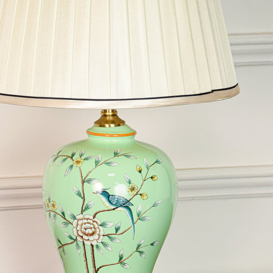 Closeup of green ceramic table lamp showing detailed hand painted floral bird pattern smooth glaze finish and brass metal base.