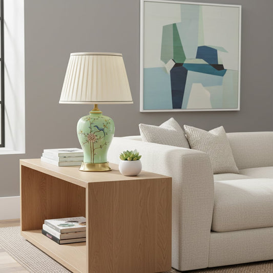 Green ceramic table lamp with hand painted floral bird design brass base and fabric shade styled on bedside or living room table.