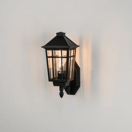 Black aluminum outdoor wall light on white background with tapered paneled clear glass shade for patio path decor.