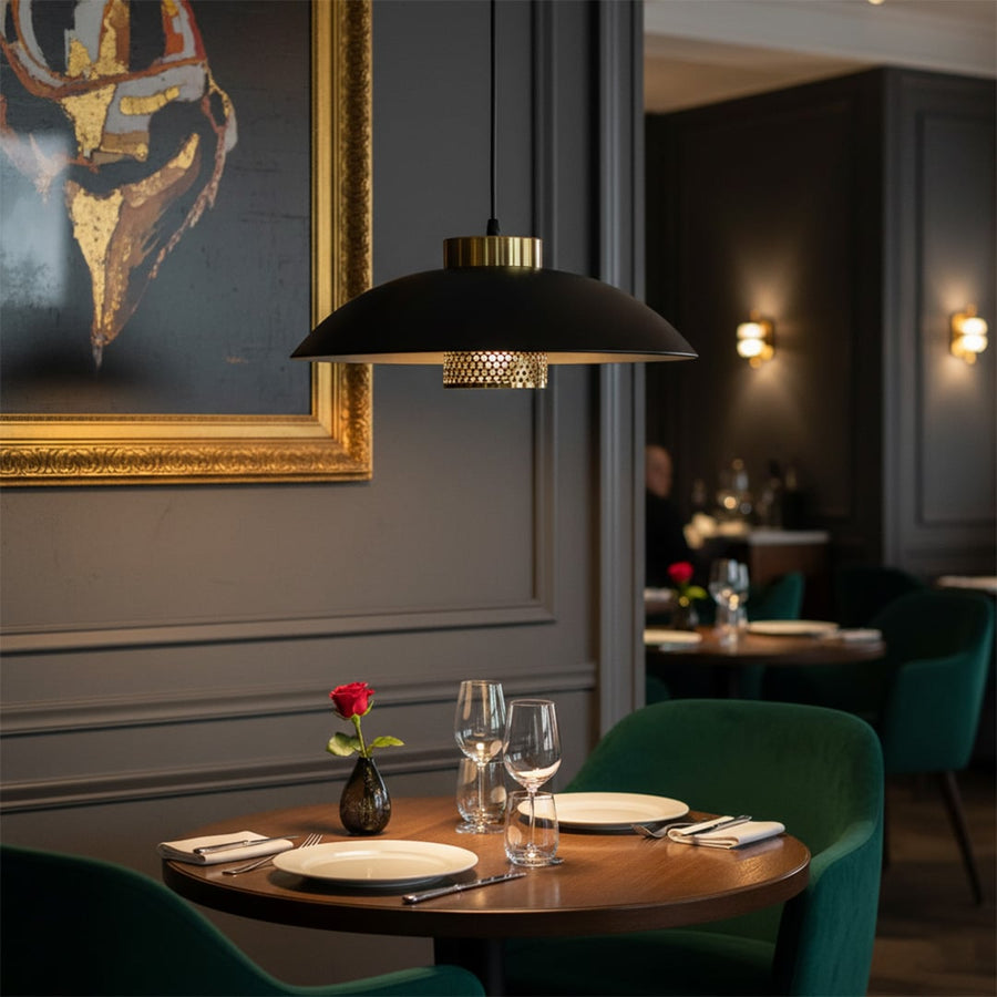 Black metal pendant light with gold detailing illuminating intimate restaurant dining table with elegant tableware and soft ambient mood lighting.