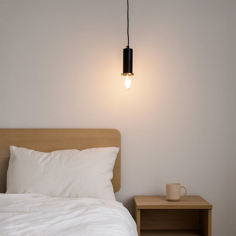 Black metal pendant light hanging beside a wooden bed creating warm ambient lighting for a modern minimalist bedroom interior.