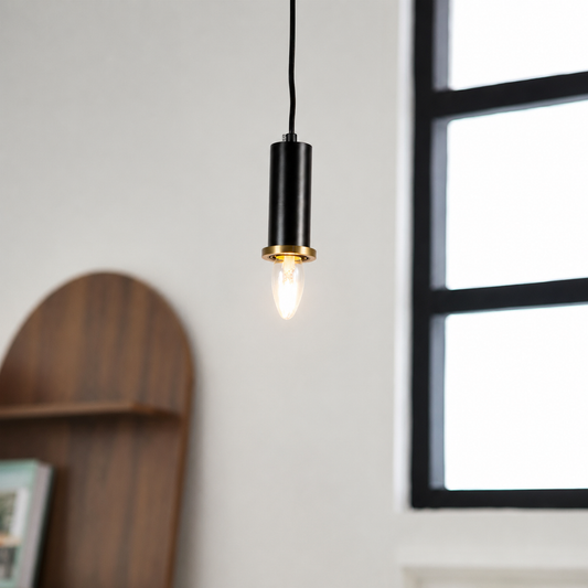 A modern black pendant light with a gold accent ring and a glowing bulb, hanging in a bright room next to a window.