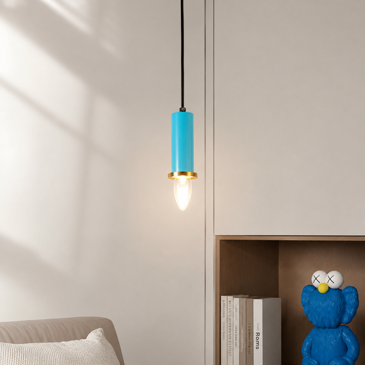 A modern pendant light with a bright blue cylindrical shade and a gold metal accent, hanging in a minimalist room next to a shelf with books and a blue toy figure.