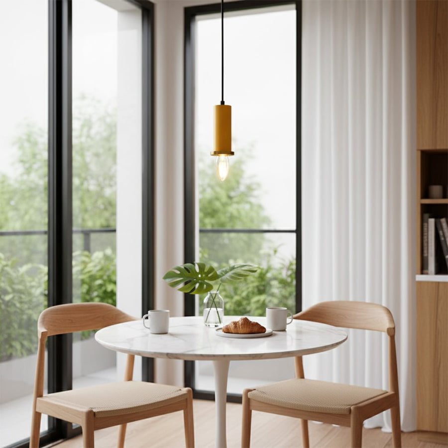 Yellow metal pendant light hanging above a round dining table creating warm ambient lighting in a modern sunlit dining space.
