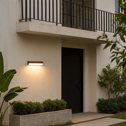 Modern black linear outdoor wall light emitting warm downward glow on white modern exterior wall above a concrete planter.