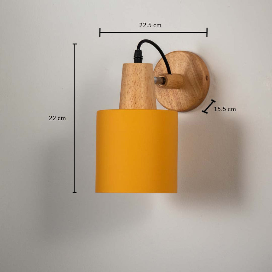 Wall lamp with matte mustard yellow cylinder shade wooden base and black cord shown with size 22 cm height 22.5 cm width and 15.5 cm depth.