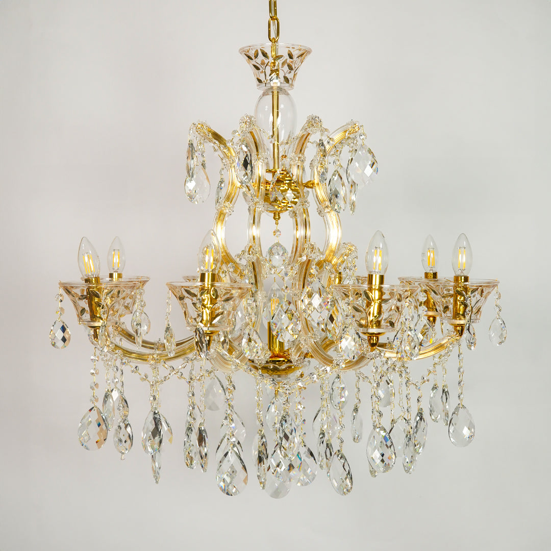 A multi-arm gold-finished crystal chandelier with hanging teardrop prisms and candle-style bulbs, shown against a plain light gray background.