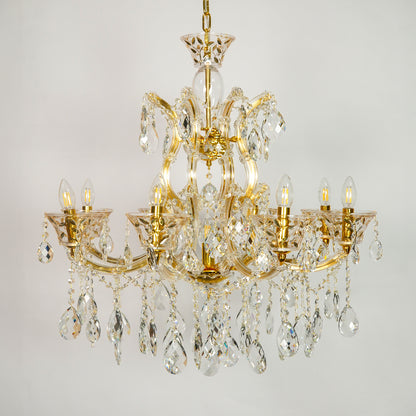 A multi-arm gold-finished crystal chandelier with hanging teardrop prisms and candle-style bulbs, shown against a plain light gray background.