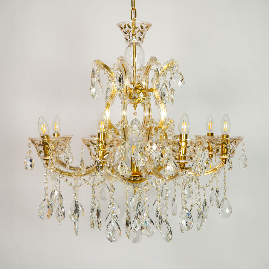 A multi-arm gold-finished crystal chandelier with hanging teardrop prisms and candle-style bulbs, shown against a plain light gray background.