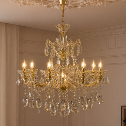 An ornate gold and clear crystal chandelier hanging from a decorative ceiling in an elegant room with beige walls and curtains.