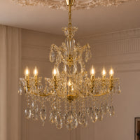 An ornate gold and clear crystal chandelier hanging from a decorative ceiling in an elegant room with beige walls and curtains.