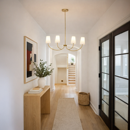 Gold metal chandelier with fabric drum shades creating warm ambient lighting in a modern hallway with elegant decor.