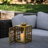 Modern gold metal candle lantern with glass panels placed on a patio table adding elegant outdoor ambient lighting.