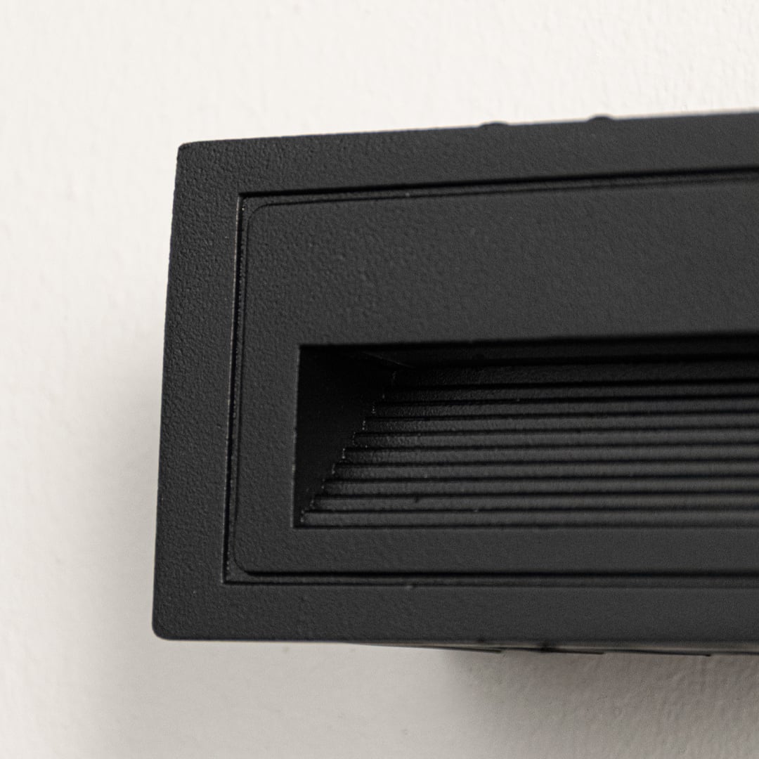 Closeup of black outdoor wall light showing recessed vent design textured metal finish and durable weather resistant construction.