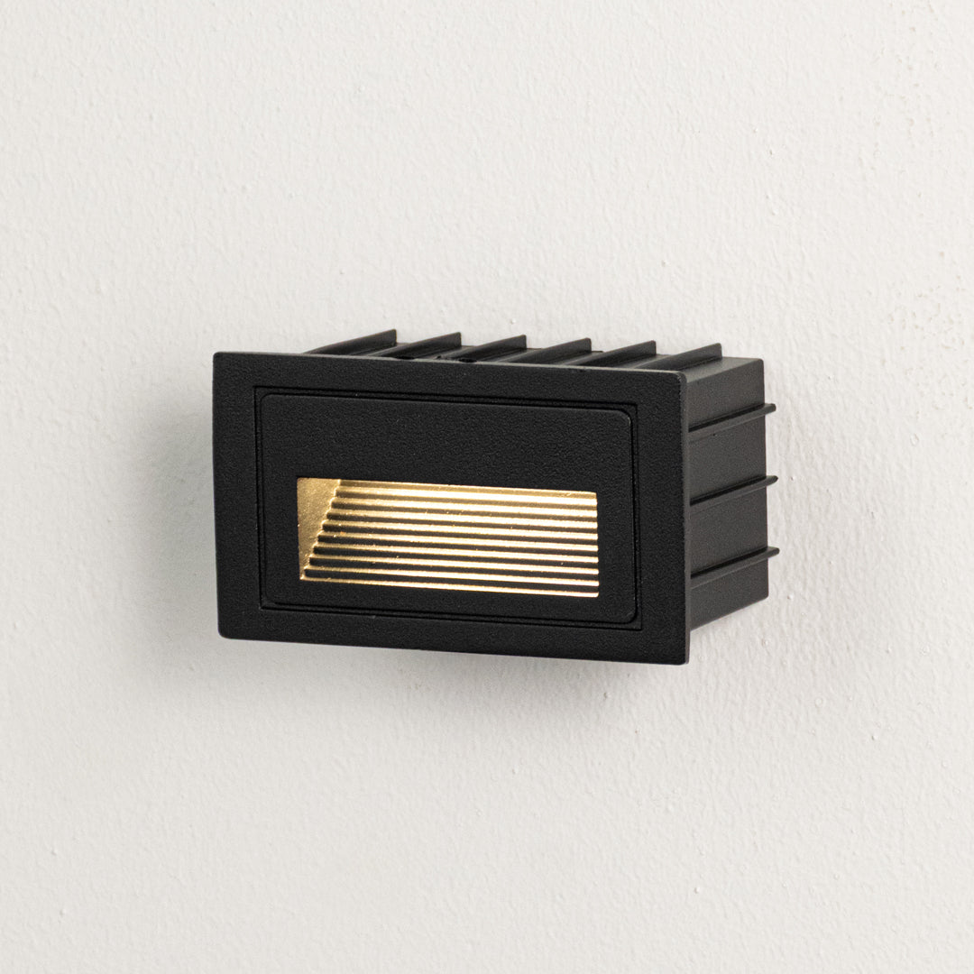 Black metal outdoor wall light on white background with louvered warm lighting for minimalist patio decor.