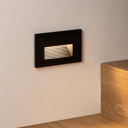 Black recessed step light illuminating staircase wall with soft ambient glow for modern architectural lighting.