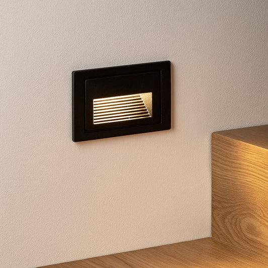 Black recessed step light illuminating staircase wall with soft ambient glow for modern architectural lighting.