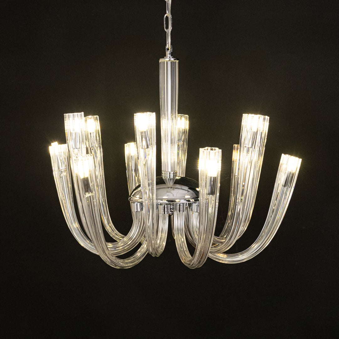 Modern chrome and clear glass chandelier glowing warmly on black background creating a striking modern ceiling feature.