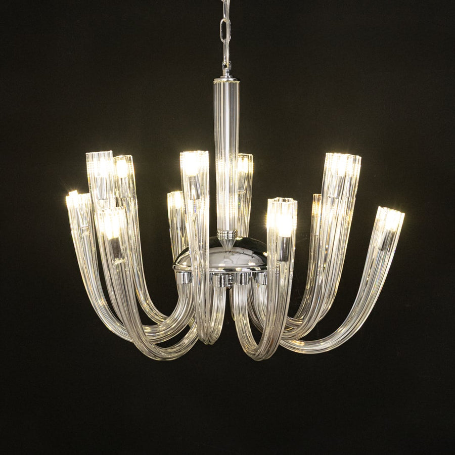 Modern chrome and clear glass chandelier glowing warmly on black background creating a striking modern ceiling feature.