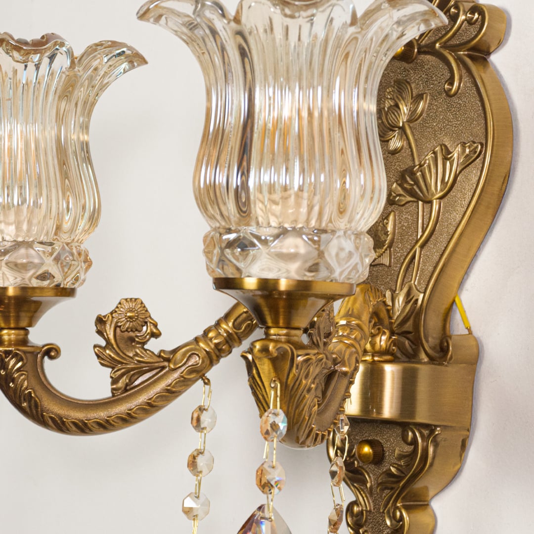 Closeup of antique gold wall light showing floral metal detailing and ribbed amber glass shades for refined interior decor.