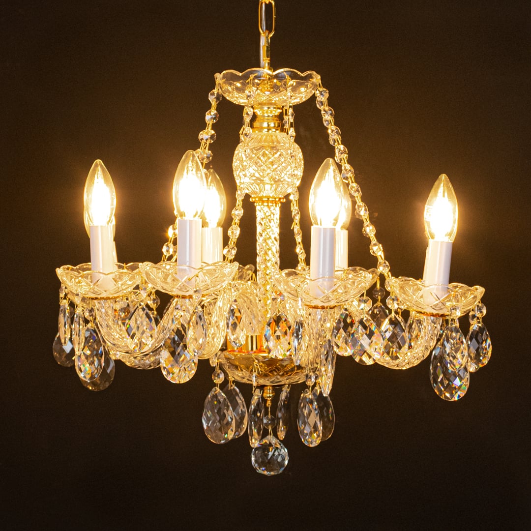Gold metal crystal chandelier glowing warmly on black background creating a dramatic luxury ceiling feature.